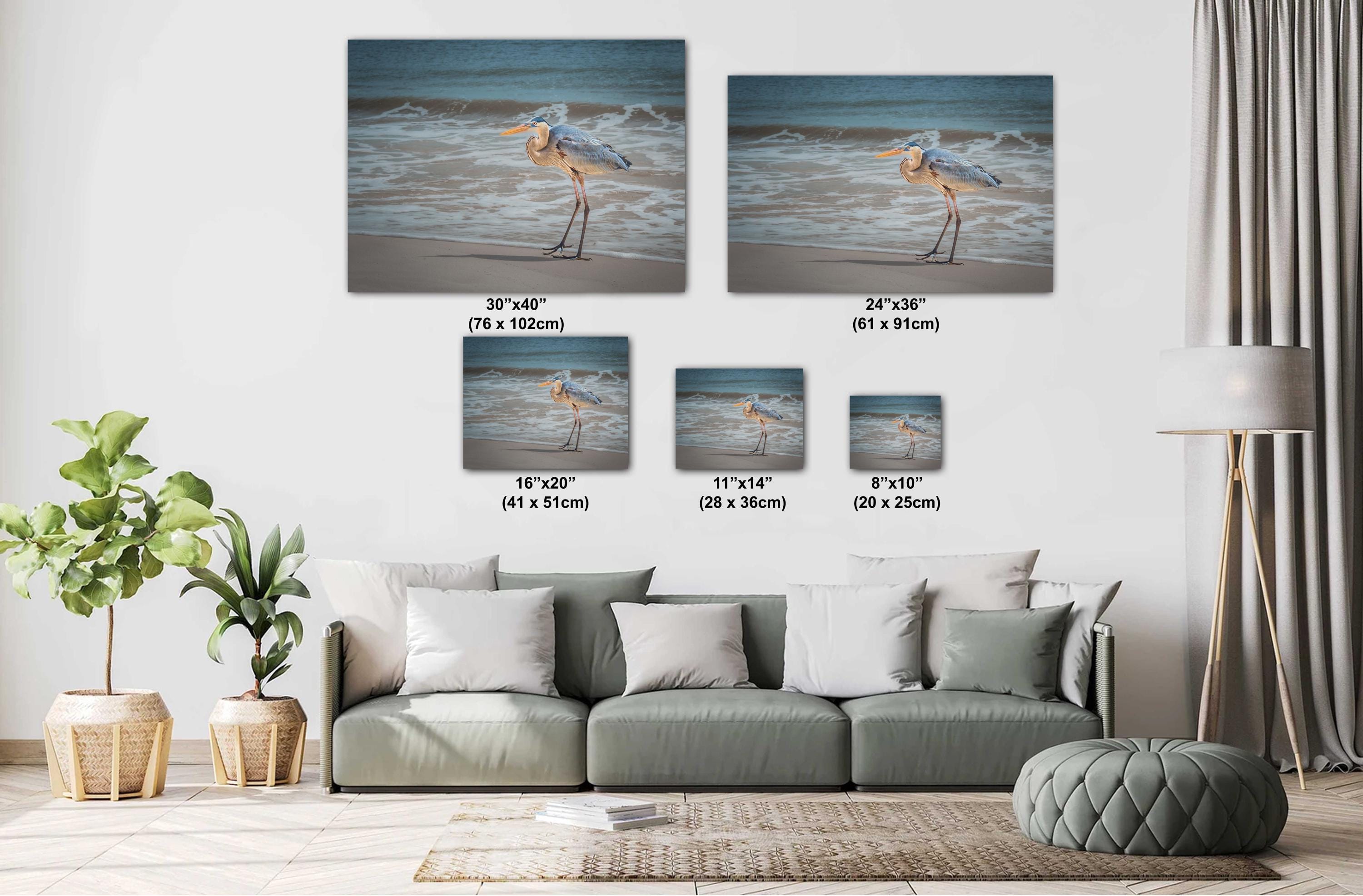 A wall art print featuring a great blue heron standing on a beach with the ocean in the background.
