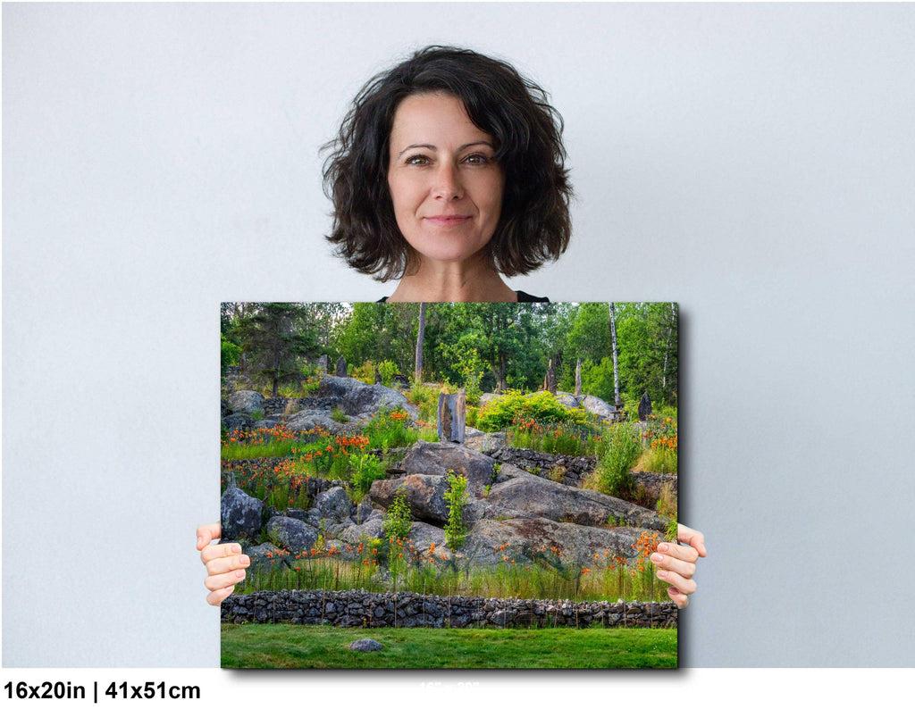 Woman holding a canvas print of a nature scene with rocks and greenery.
