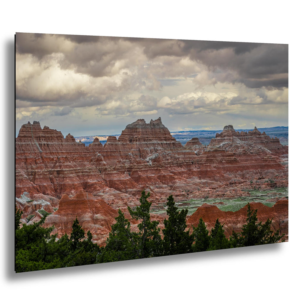 Badlands National Park red rock formations under storm clouds with green pines in the foreground