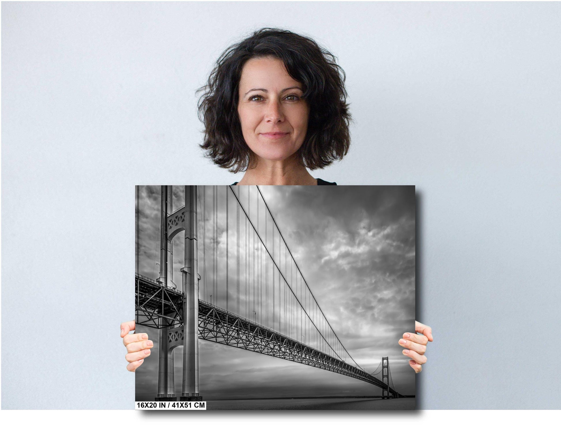 A black and white photograph of the Mackinac Bridge, capturing the engineering and grandeur of the structure with a backdrop of overcast sky and a body of water.