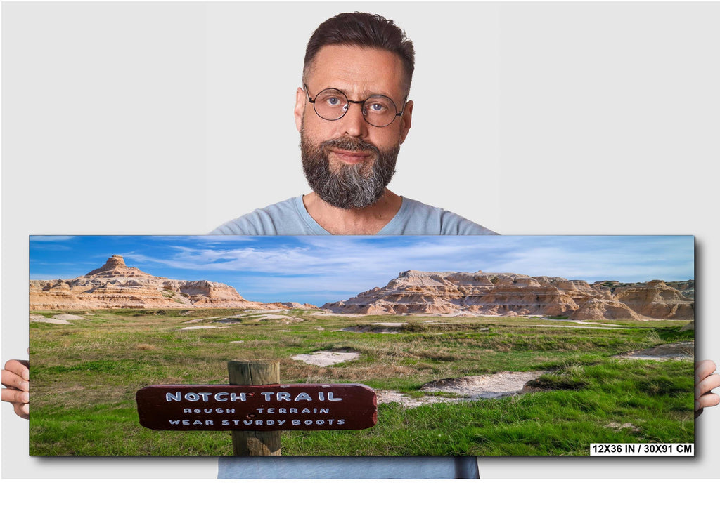 Man holding a panoramic landscape print of a scenic trail sign.