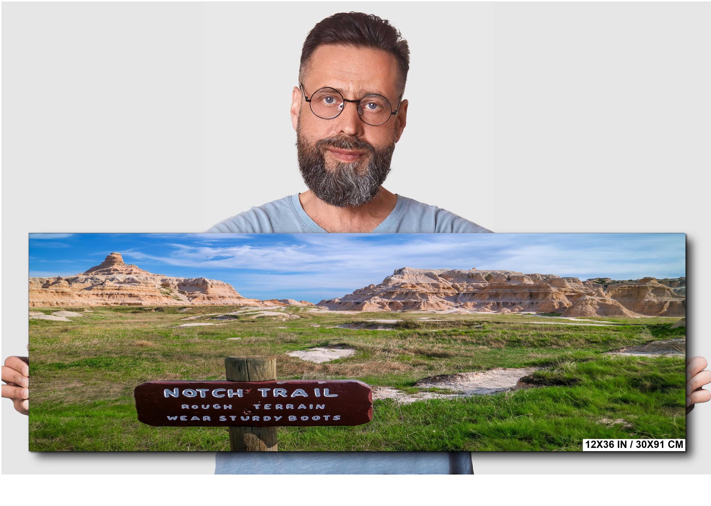 Man holding a panoramic landscape print of a scenic trail sign.