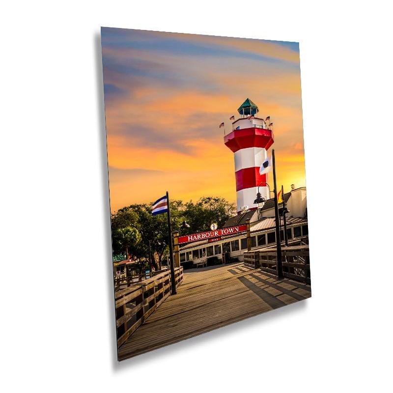 A wall art print featuring the Harbour Town Lighthouse in Hilton Head Island, South Carolina, with a red and white striped tower visible against a sunset sky.