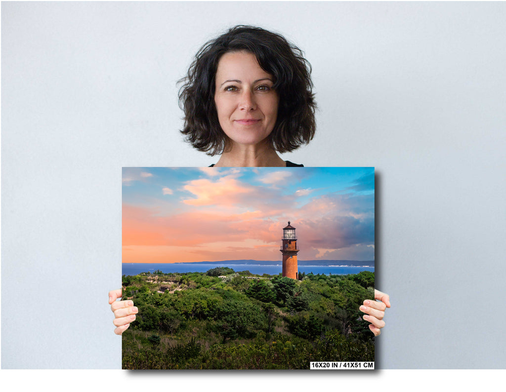 Woman holding a canvas print of a lighthouse at sunset.