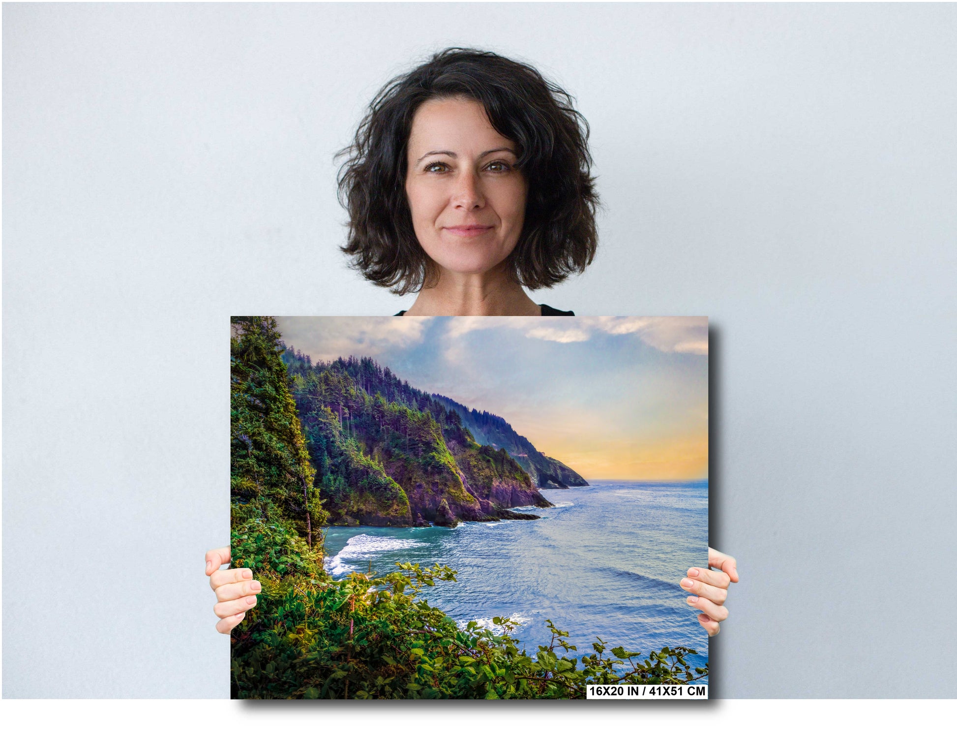 Woman holding a painting of a scenic Hart's Cove landscape with mountains and water at Rocky Oregon Coast.