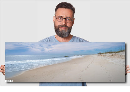 A wall art print featuring a beach scene with footprints on the sand, the ocean, and a clear sky.