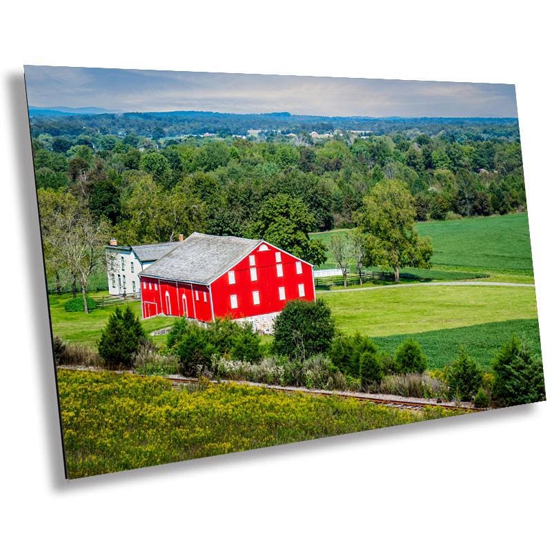 A wall art print featuring a red barn in a rural landscape with green fields and trees in McLean Farm in Adams County, Pennsylvania