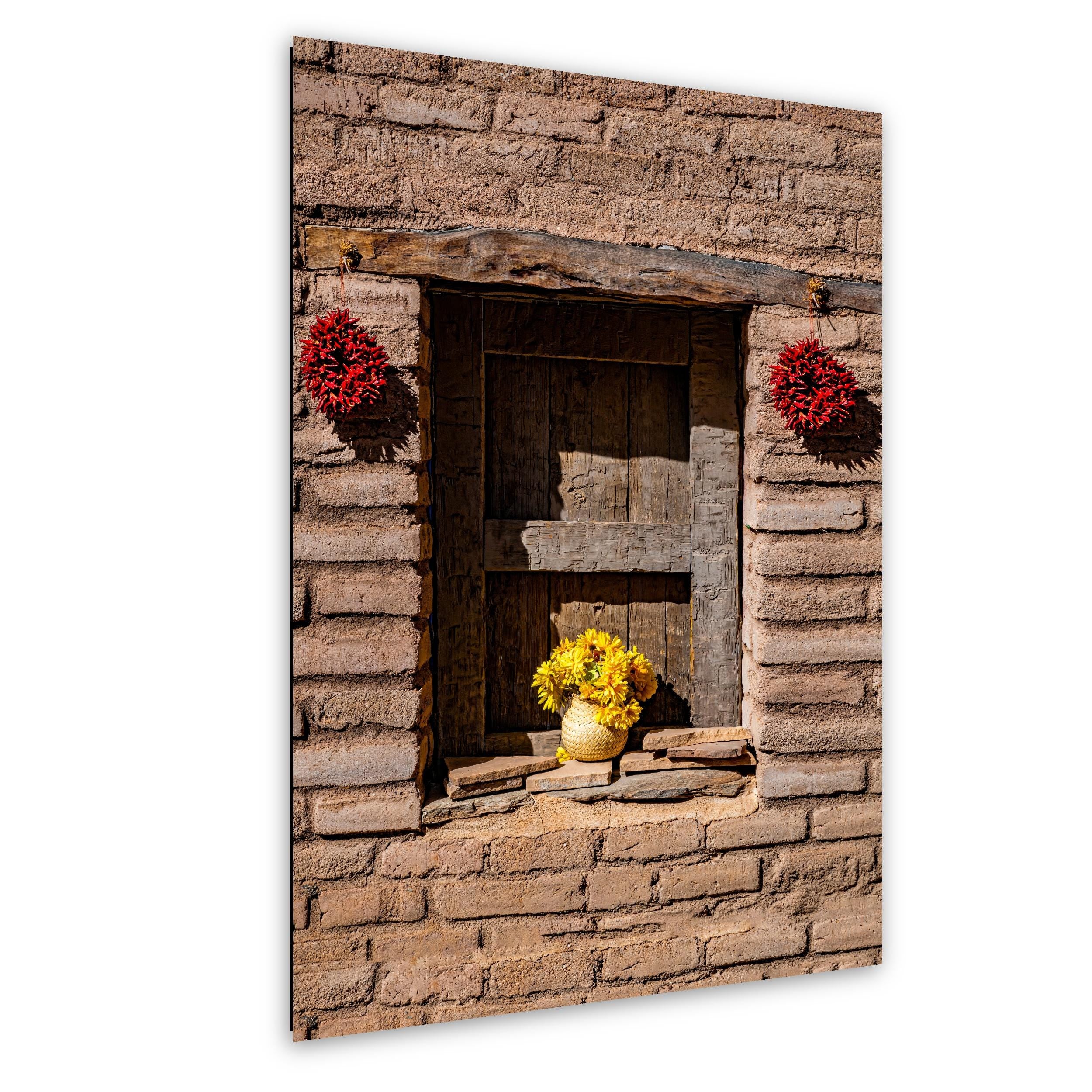 Adobe wall with wooden window, red chili ristras, and vase of yellow flowers in Southwest rustic style