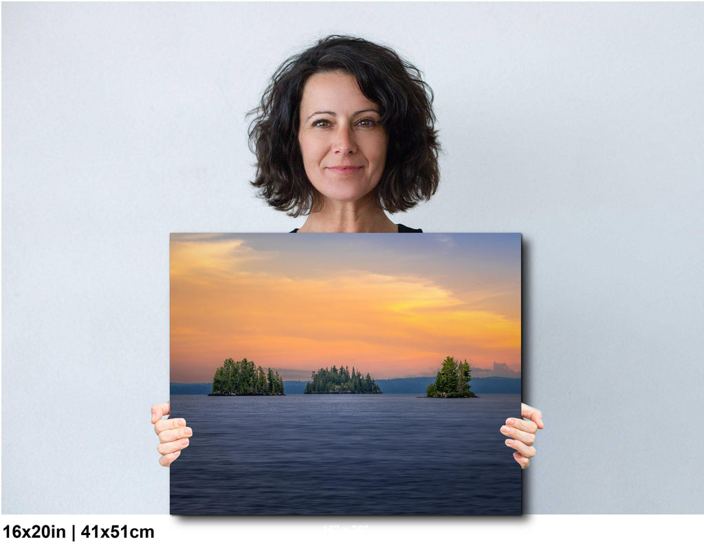 Woman holding a large photo of a sunset over water with islands.