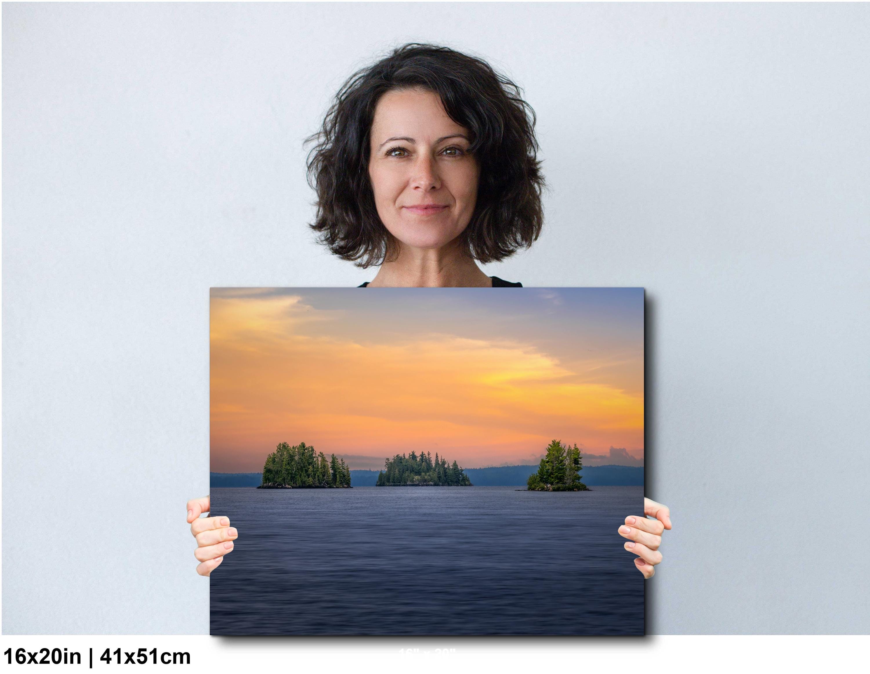 Woman holding a large photo of a sunset over water with islands.