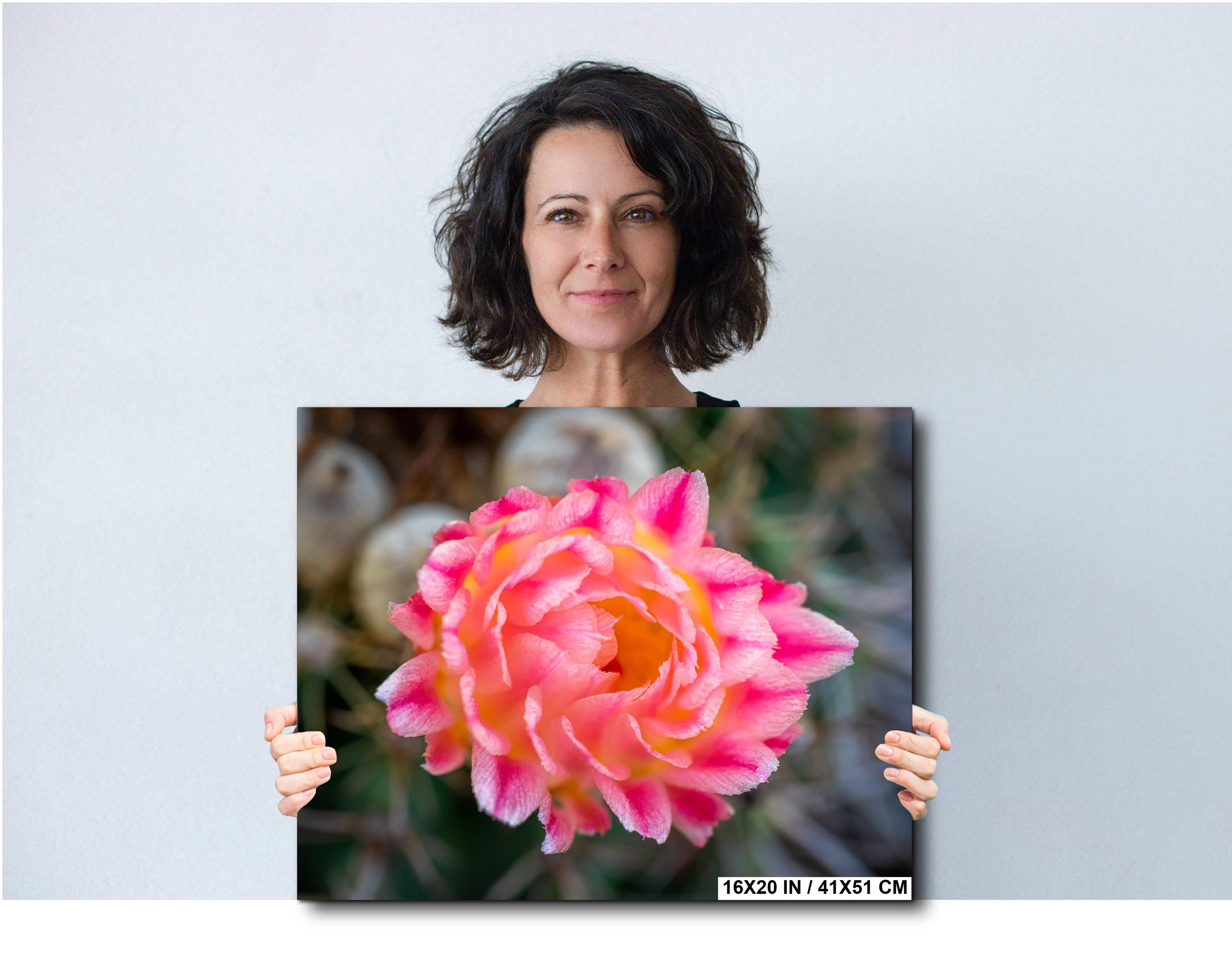 Woman holding a large print of a pink flower against a plain background