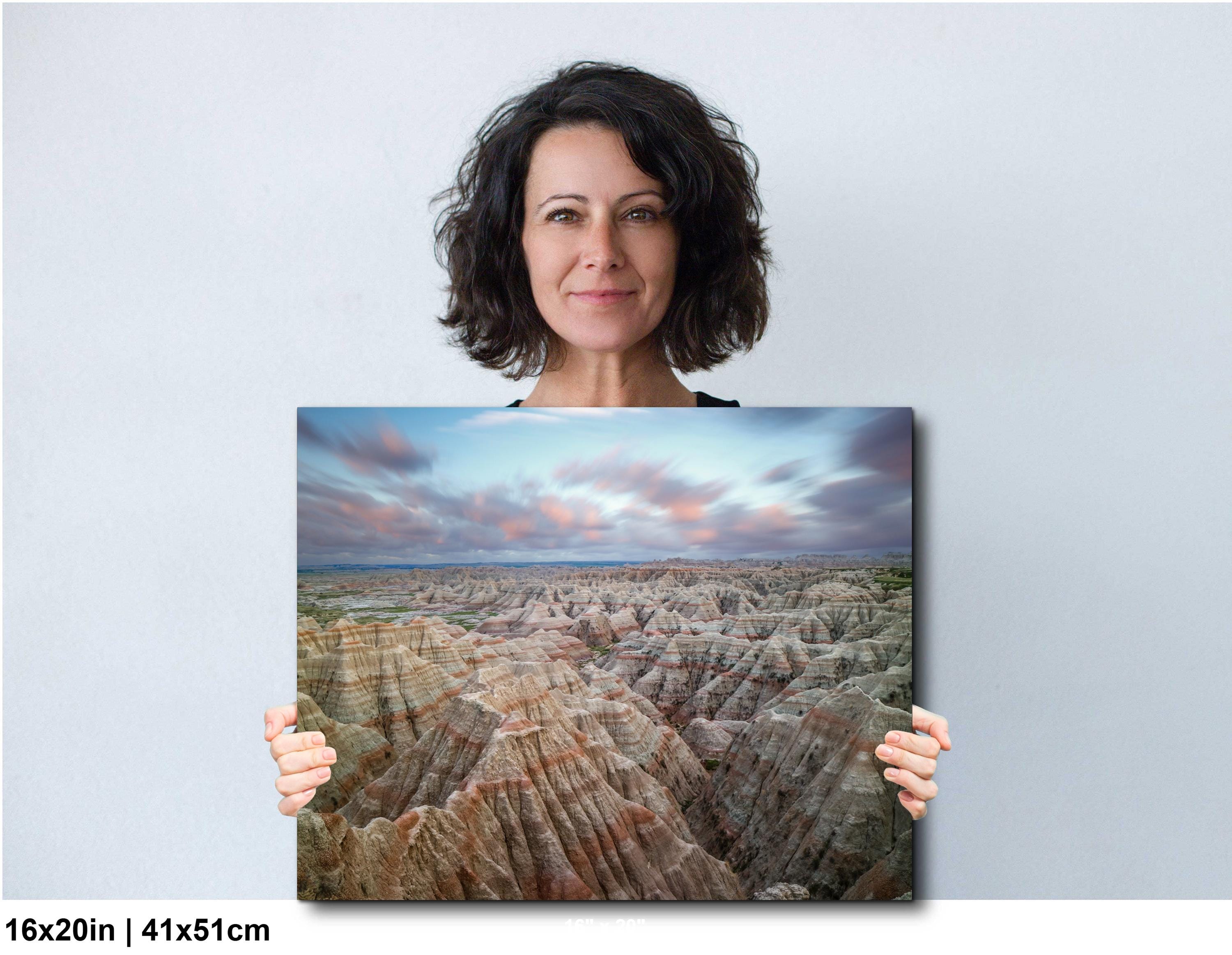 Woman holding a large landscape photo of a desert canyon with a blue sky.