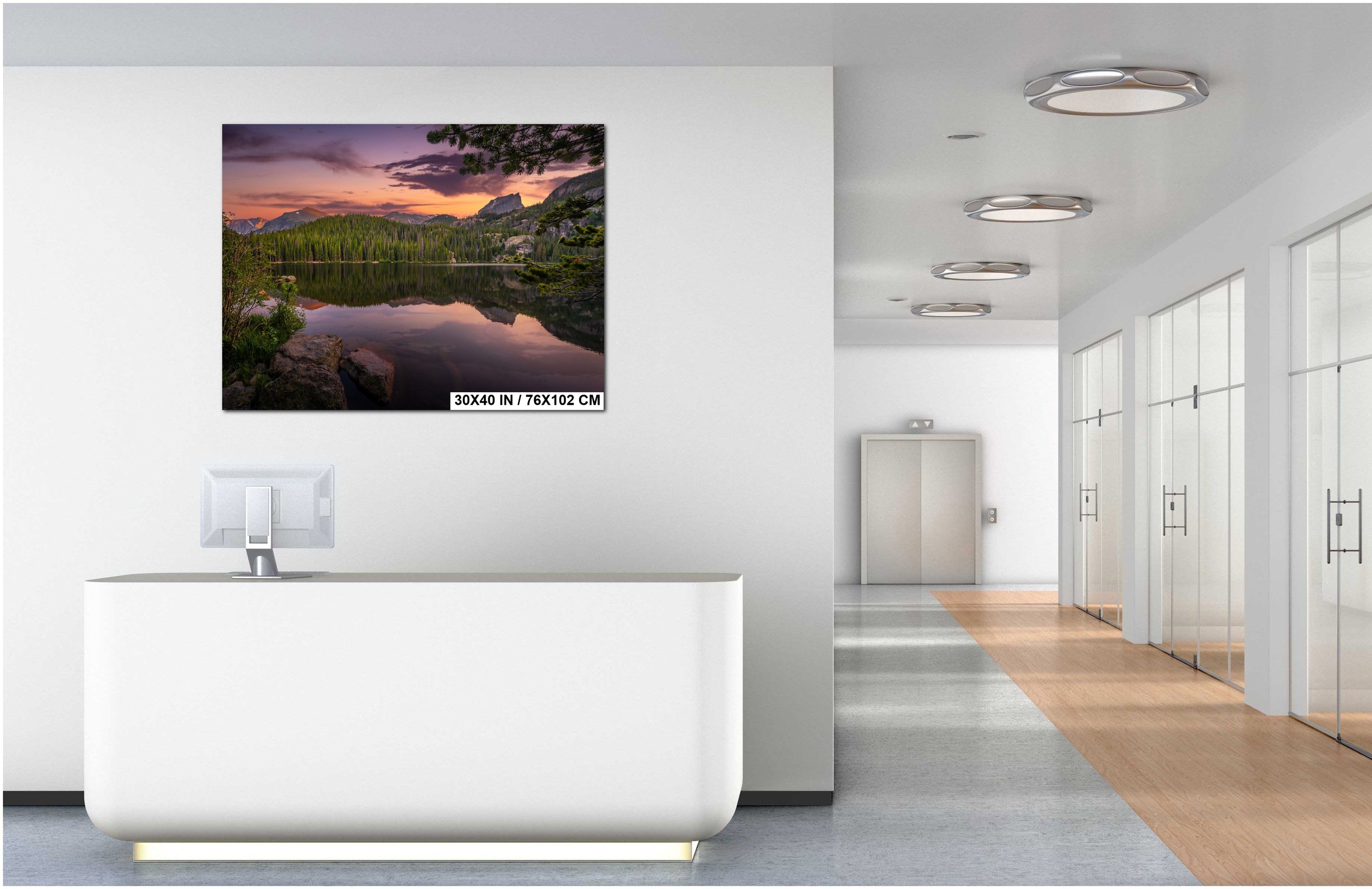 a modern office space with a large wall-mounted painting depicting a serene landscape with a lake and mountains. The painting is surrounded by a minimalist design, with a white desk and a glass partition in the foreground.