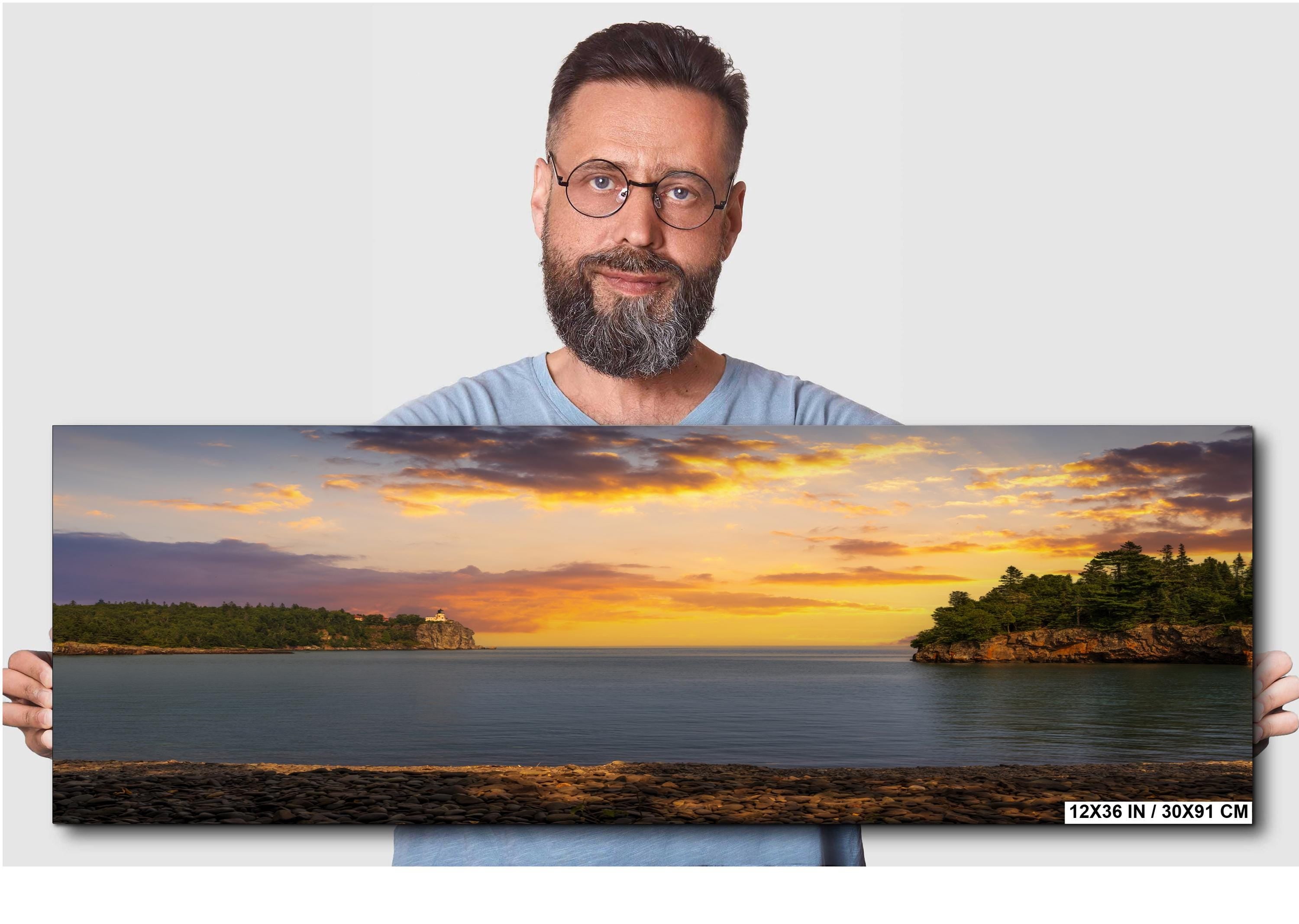 Man holding a panoramic landscape of a sunset over water
