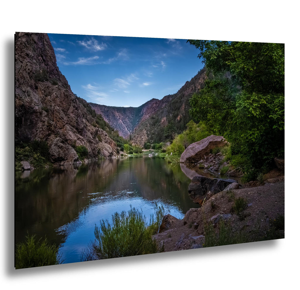 Calm Gunnison River flowing through Black Canyon with towering cliffs and lush greenery in Colorado.