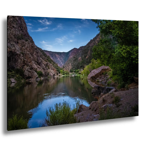 Calm Gunnison River flowing through Black Canyon with towering cliffs and lush greenery in Colorado.