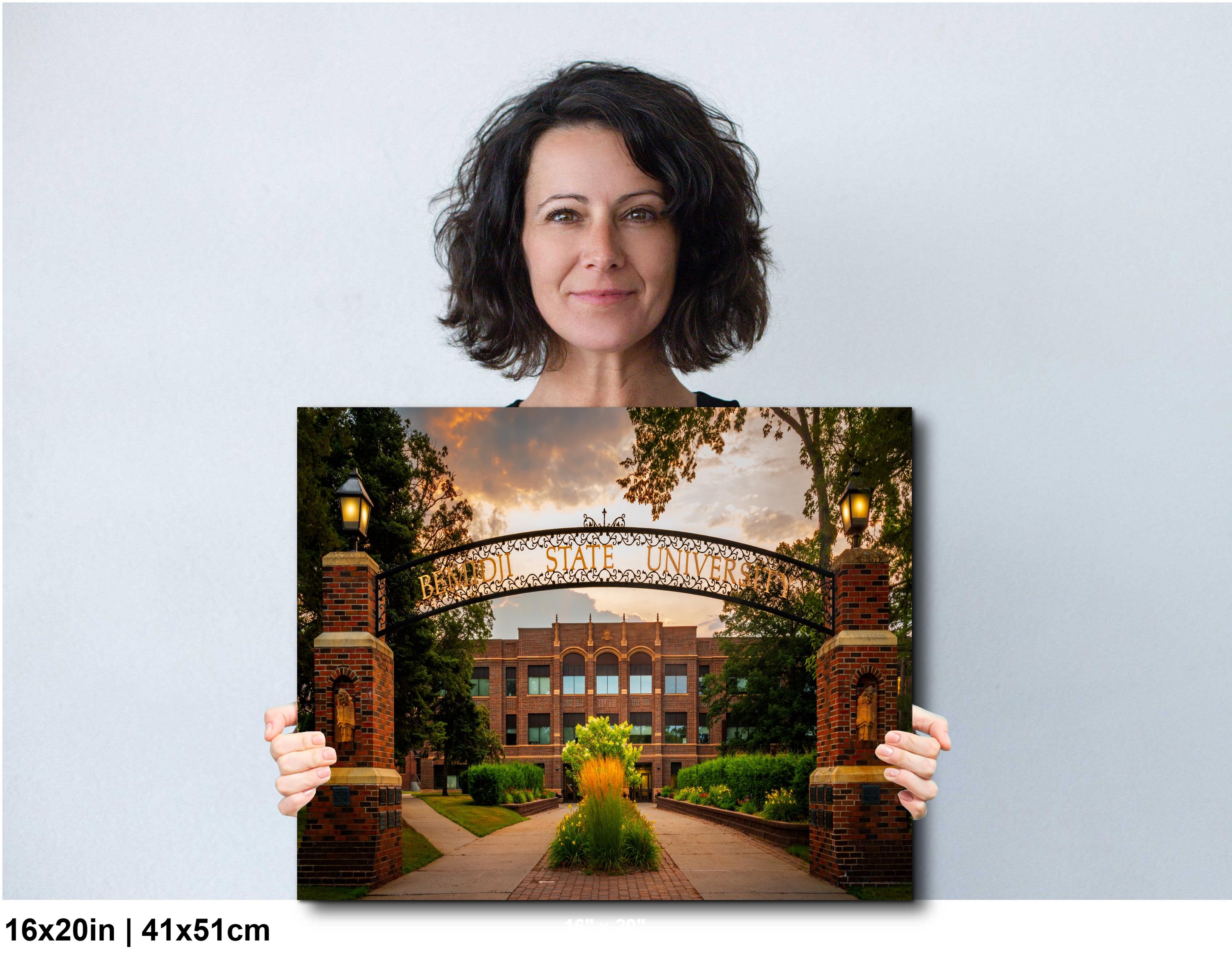 Woman holding a photograph of a university archway with 'Bemidji State University' on a light gray background.