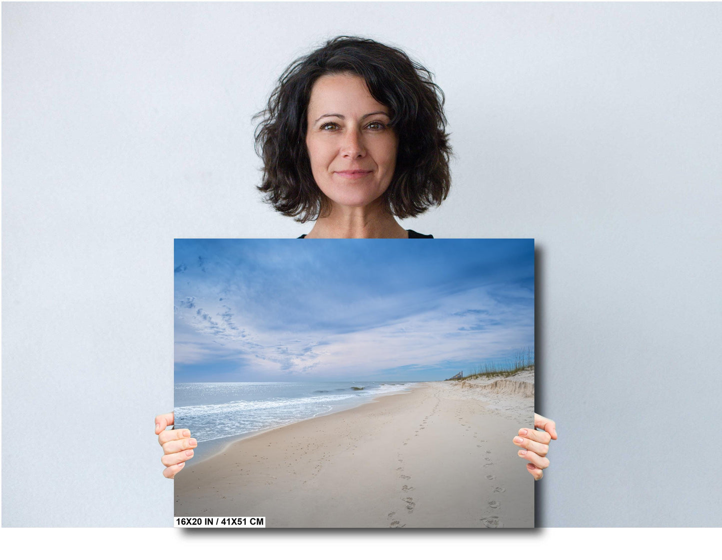 Woman holding a 16x20 beach photography canvas print of footprints in the Sands of Perdido Key.