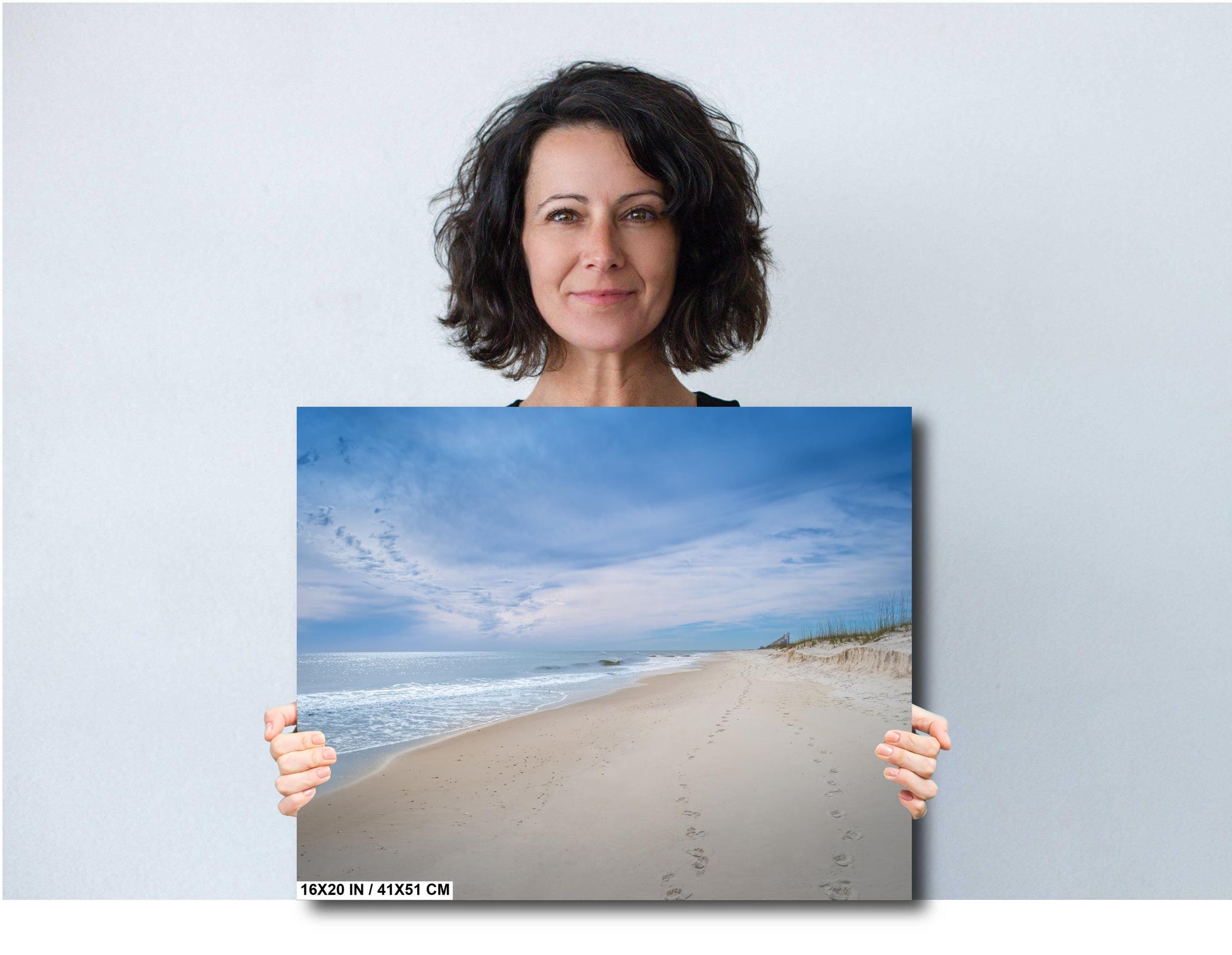 Woman holding a 16x20 beach photography canvas print of footprints in the Sands of Perdido Key.