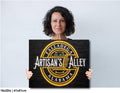 Woman holding a sign with 'Artisan's Alley' branding against a light gray background