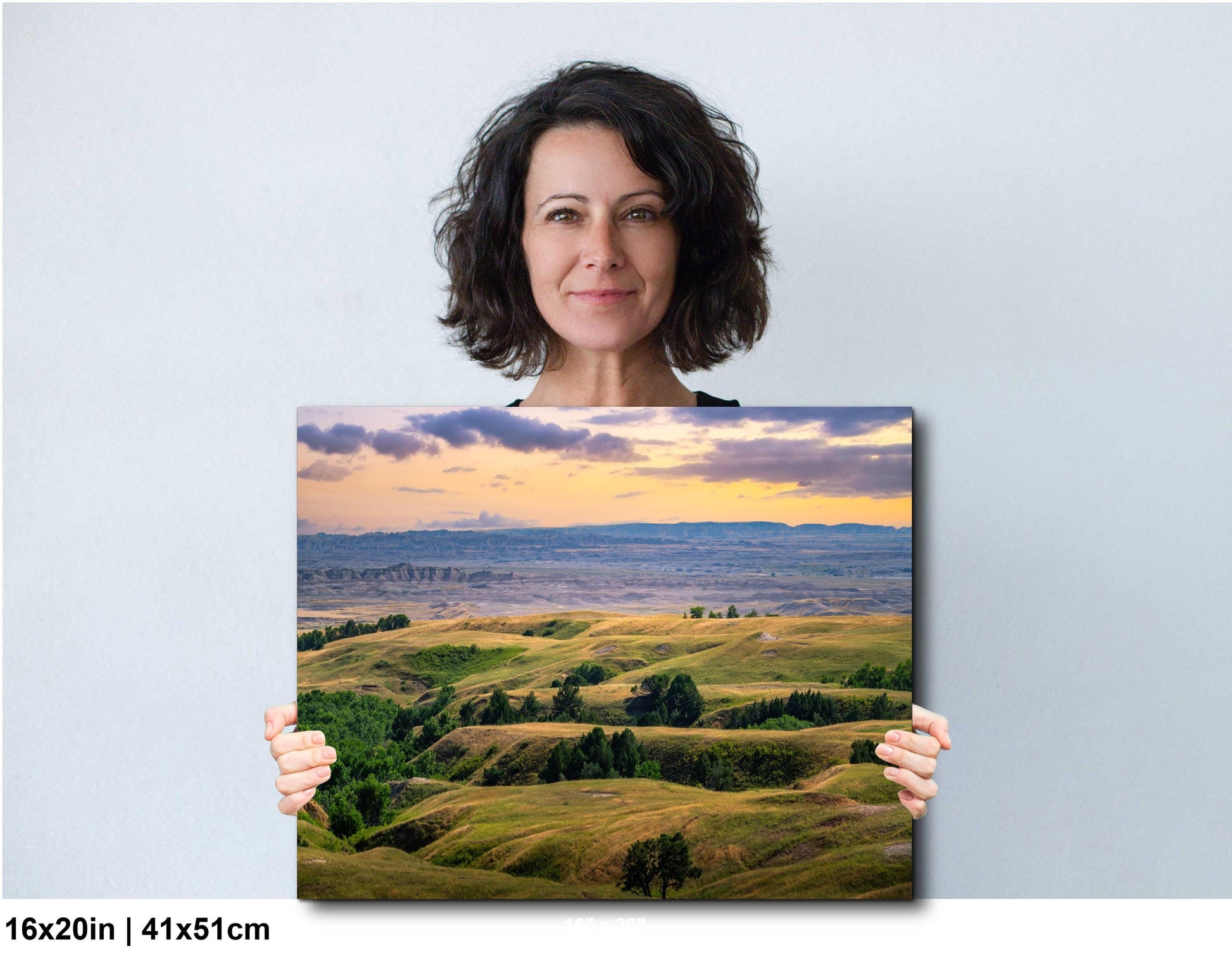 Woman holding a landscape print of rolling hills and a sunset.