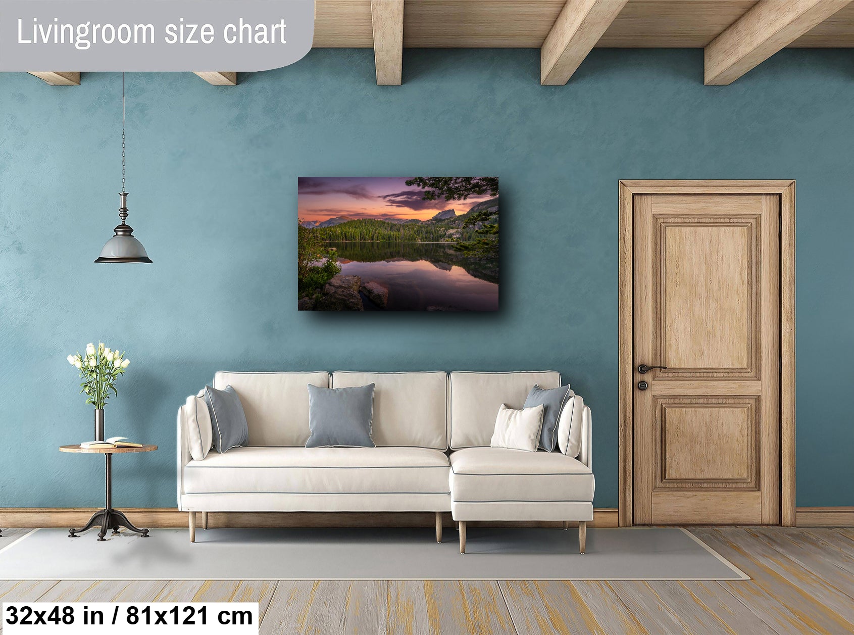 a living room with a large painting of a serene landscape hanging on the wall. The painting features a lake surrounded by mountains and trees, creating a peaceful and natural atmosphere. The room is furnished with a white sofa and a wooden door, and there is a small table with a vase of flowers nearby. The living room size chart indicates that the space is 32 inches by 61 inches, providing a scale for the viewer.