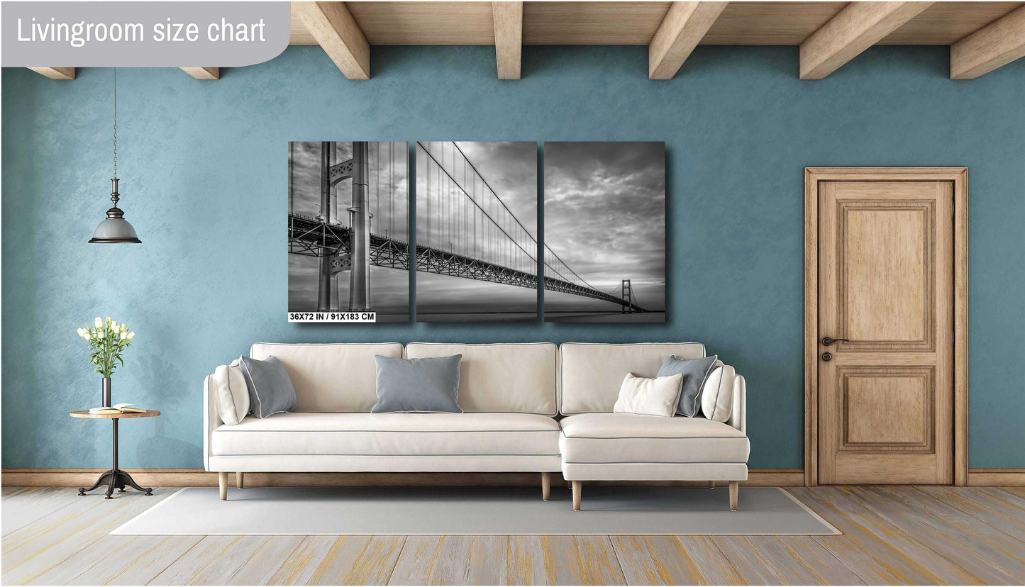 A black and white photograph of the Mackinac Bridge, capturing the engineering and grandeur of the structure with a backdrop of overcast sky and a body of water.