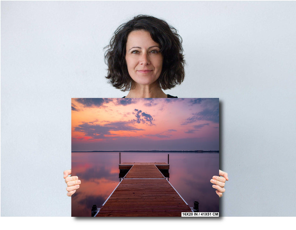 A woman holding a 16x20 inches wall art of sunset over calm Lake Bemidji with dock view and pastel skies before a summer storm.