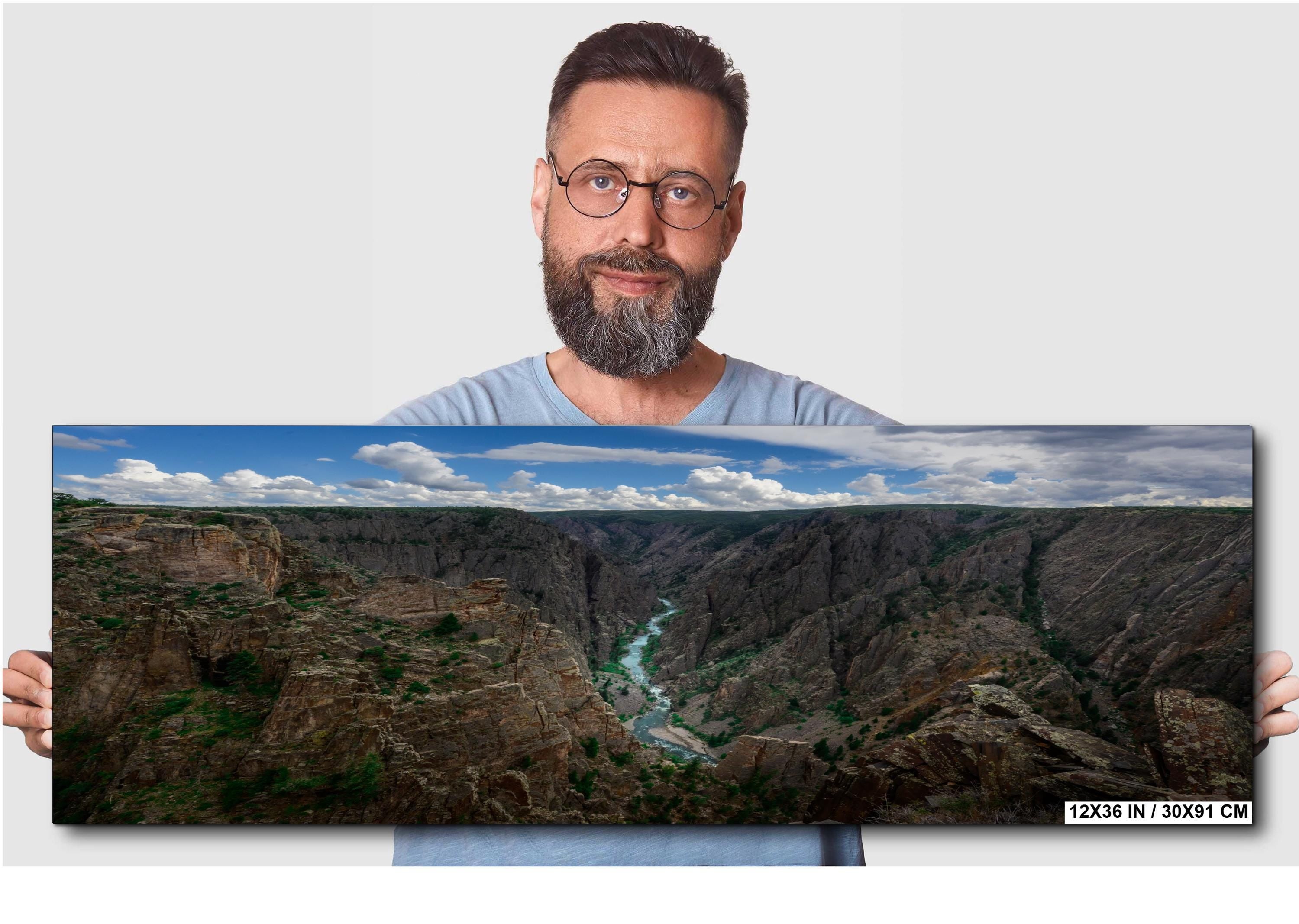 Man holding a panoramic landscape photo of a canyon with a river.