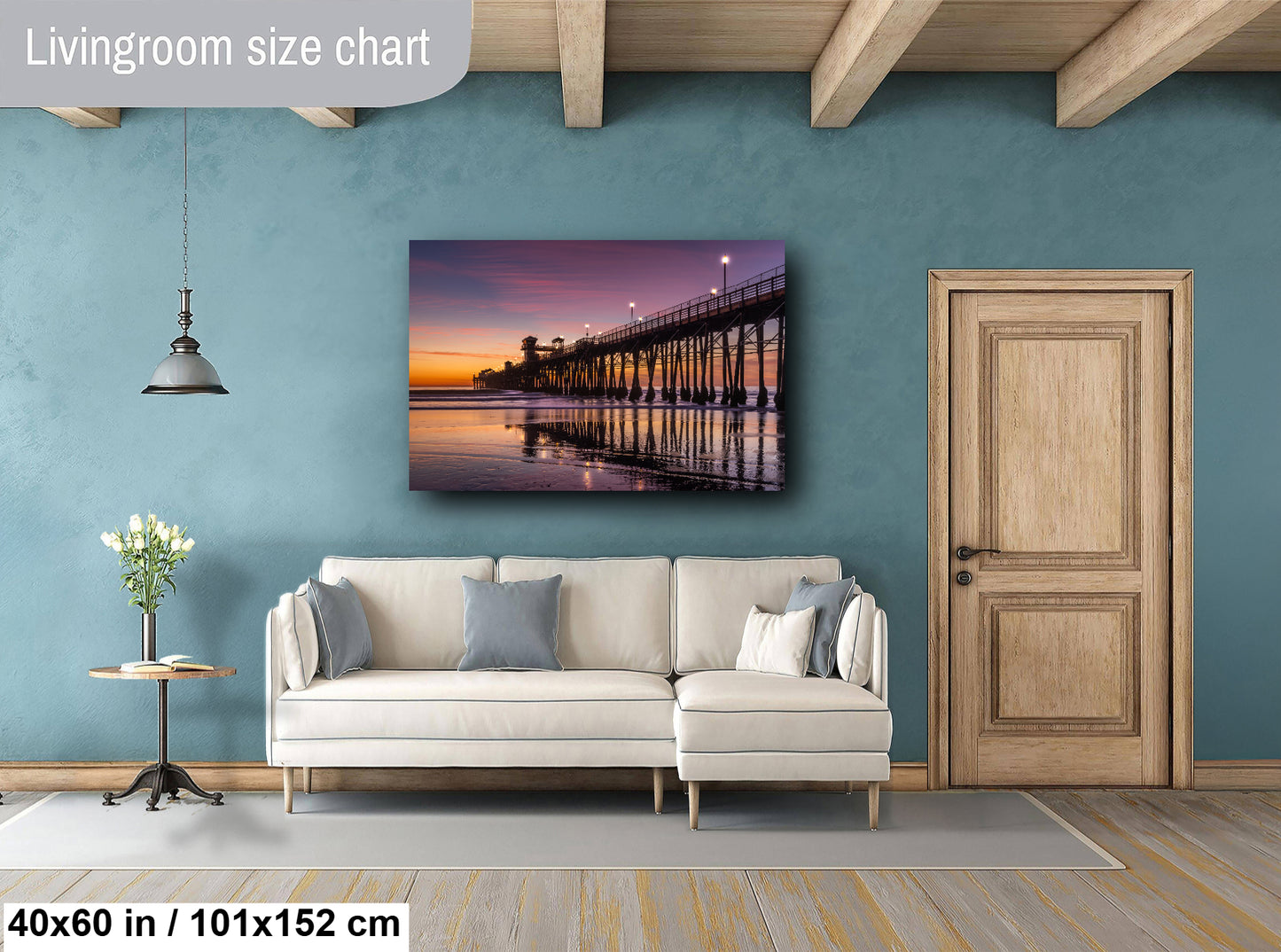 a living room with a large wall-mounted painting of a pier at sunset. The painting is framed in a white frame and hangs above a white sofa. The room has a wooden floor and a wooden door, creating a warm and cozy atmosphere.