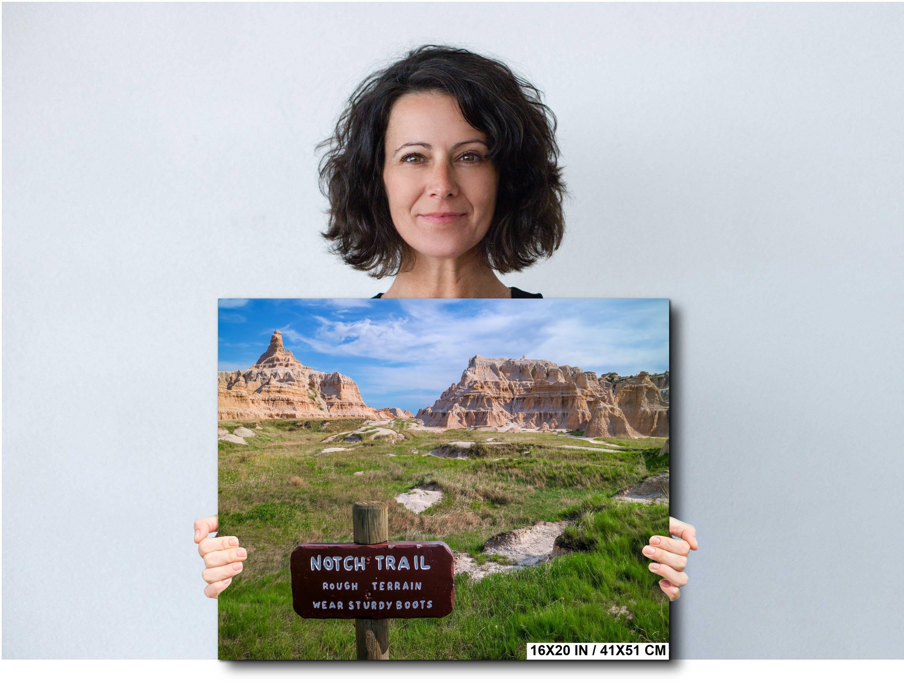 Woman holding a canvas print of a scenic landscape with a trail sign.