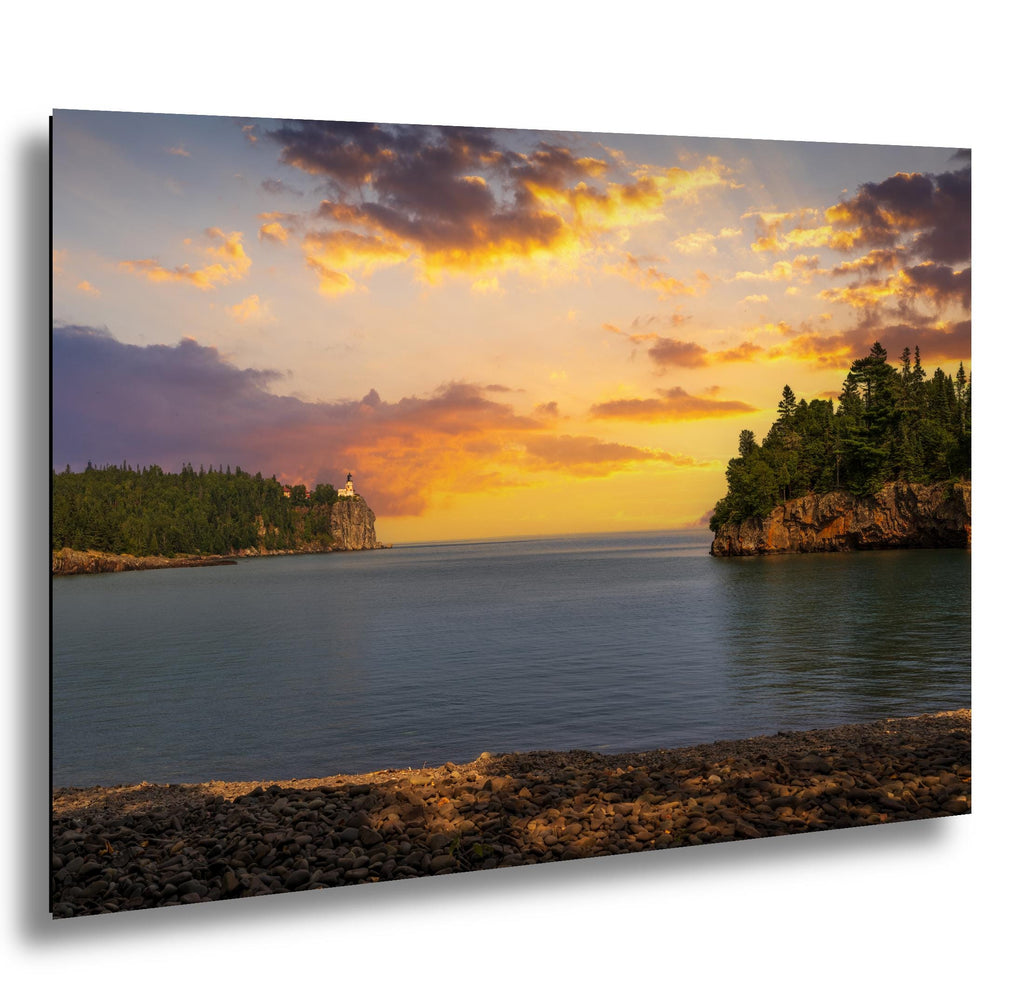 Split Rock Lighthouse at sunset above calm Lake Superior, glowing cliffs and pebble beach