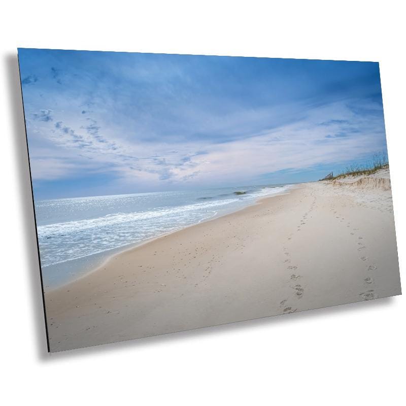 A wall art print featuring a beach scene with footprints on the sand, the ocean, and a clear sky.