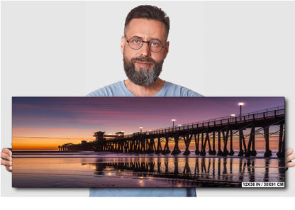 A man holding a large canvas print of a serene sunset over a pier.