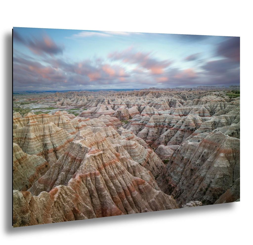 Badlands National Park layered rock formations at sunset with soft clouds above.