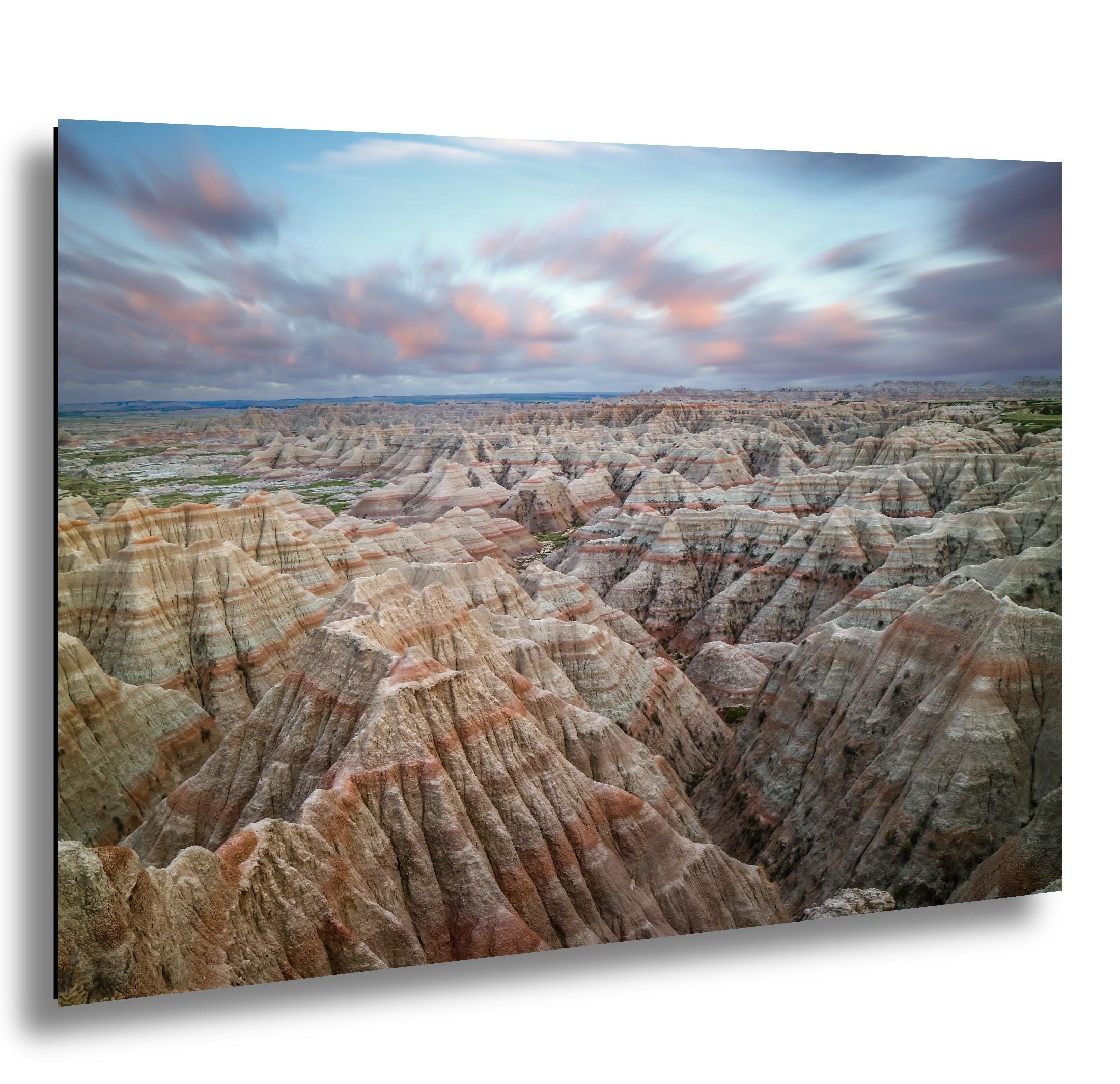Badlands National Park layered rock formations at sunset with soft clouds above.