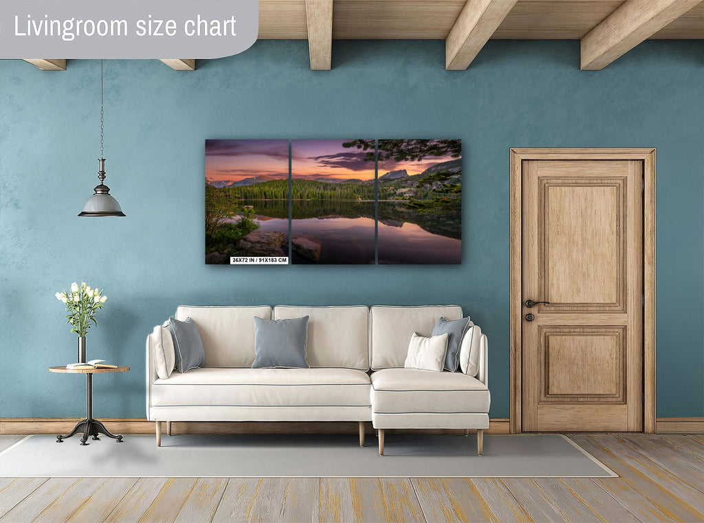 a living room with a large, three-piece sofa and a wooden door. Above the sofa, there is a large, three-piece wall art depicting a serene landscape with a lake and mountains.