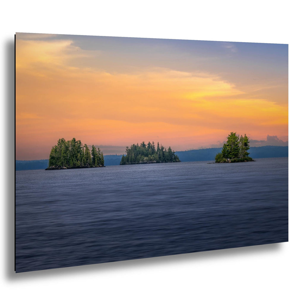 Three small islands with trees at sunset over lake islands with glowing sky in Voyageurs National Park.