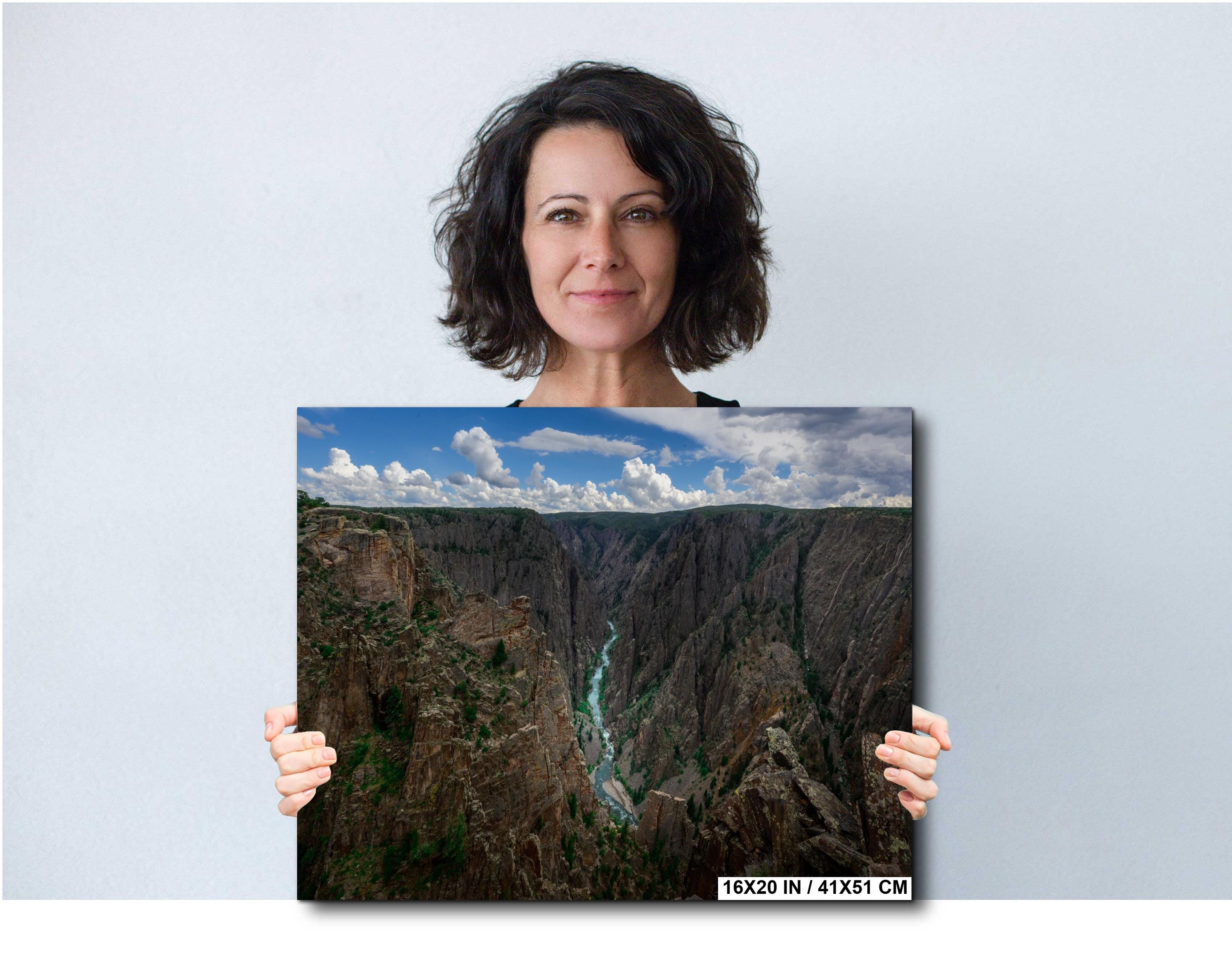Woman holding a large photograph of a canyon against a plain background