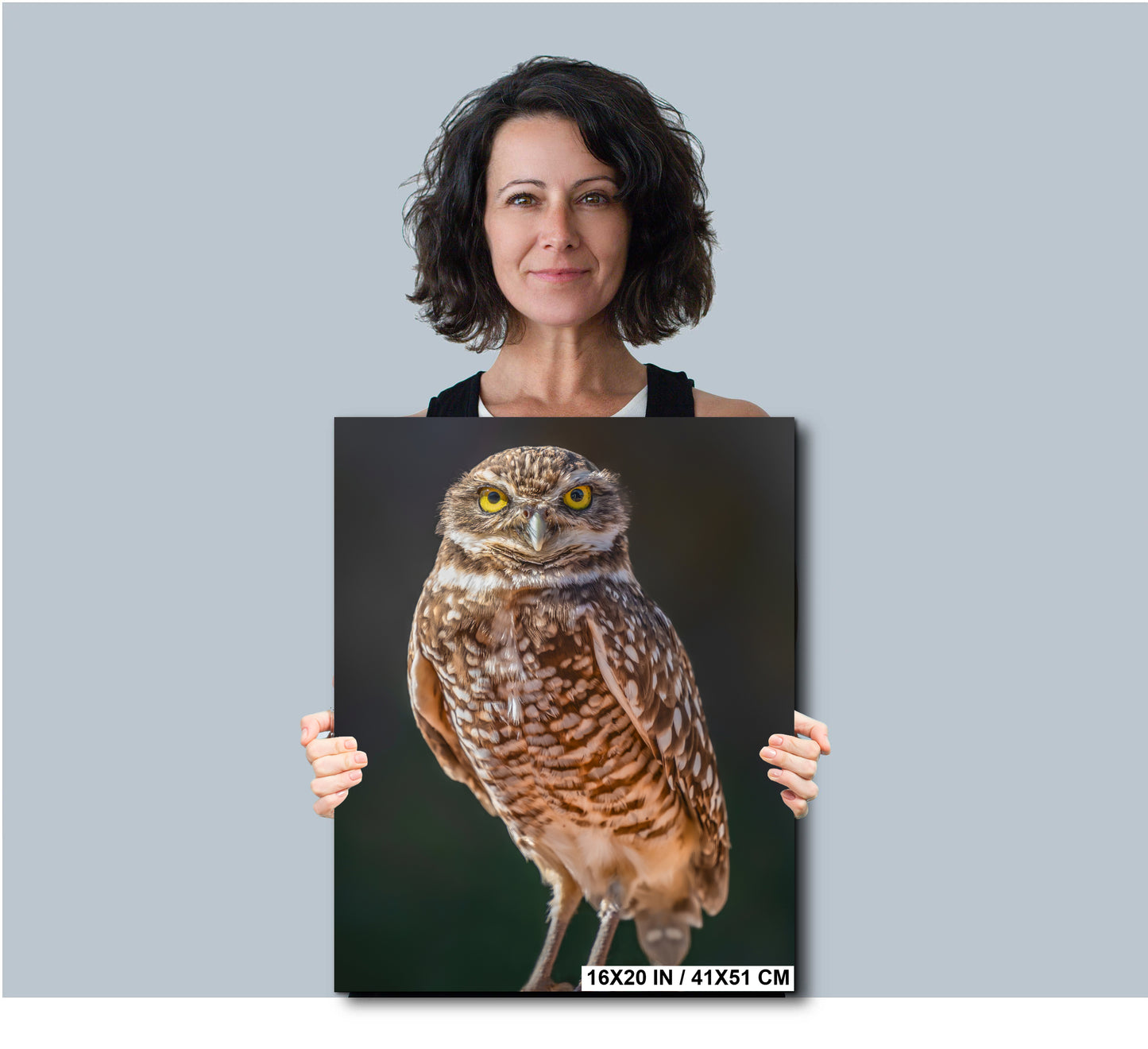 A woman is holding a framed photograph of a brown owl with yellow eyes.