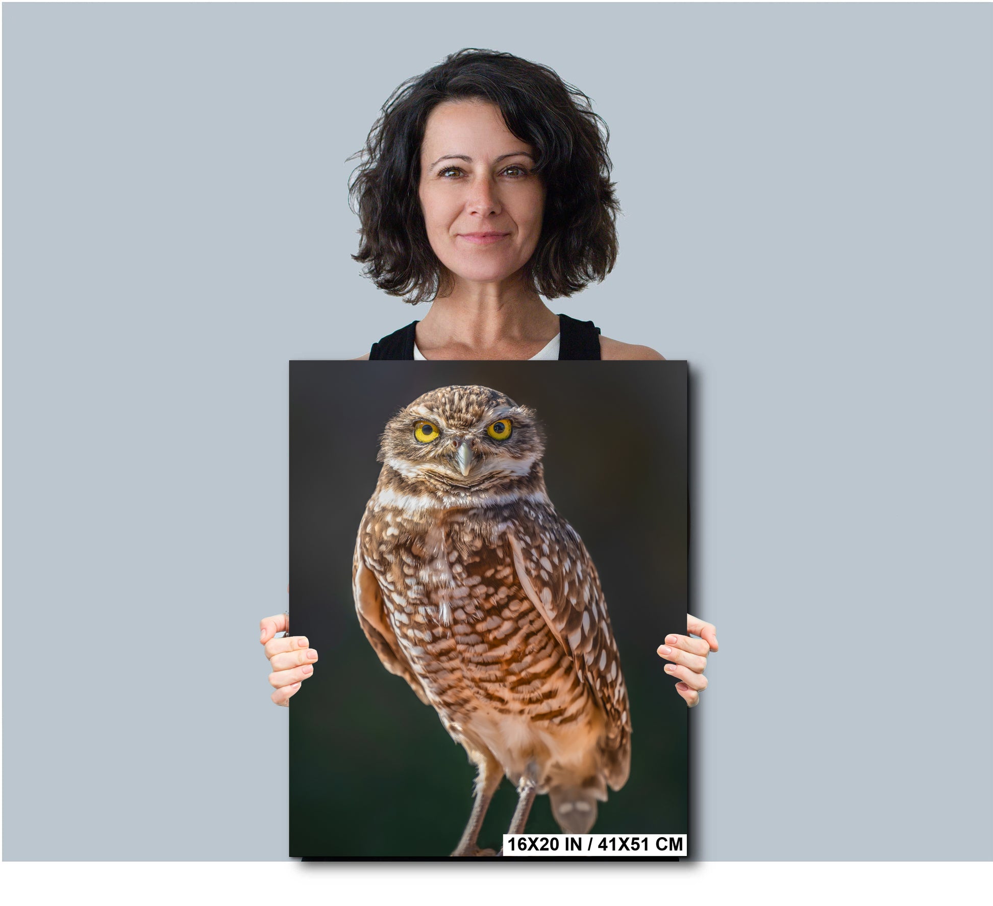 A woman is holding a framed photograph of a brown owl with yellow eyes.