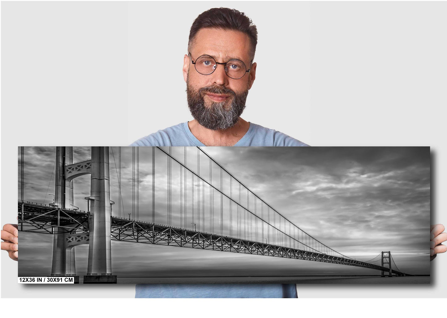 A black and white photograph of the Mackinac Bridge, capturing the engineering and grandeur of the structure with a backdrop of overcast sky and a body of water.