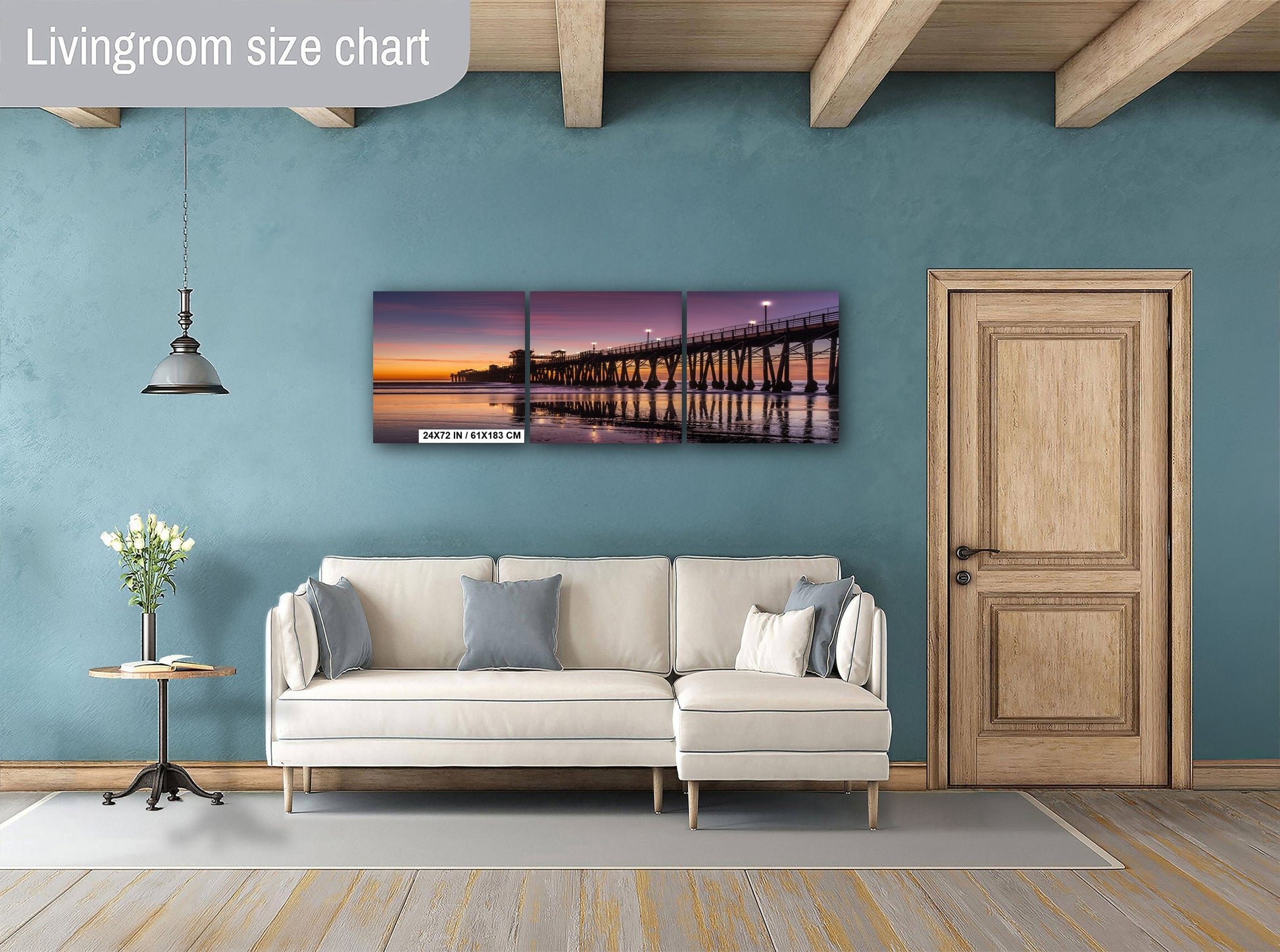 a living room with a white sofa, a wooden door, and a large wall art piece depicting a sunset over a bridge.