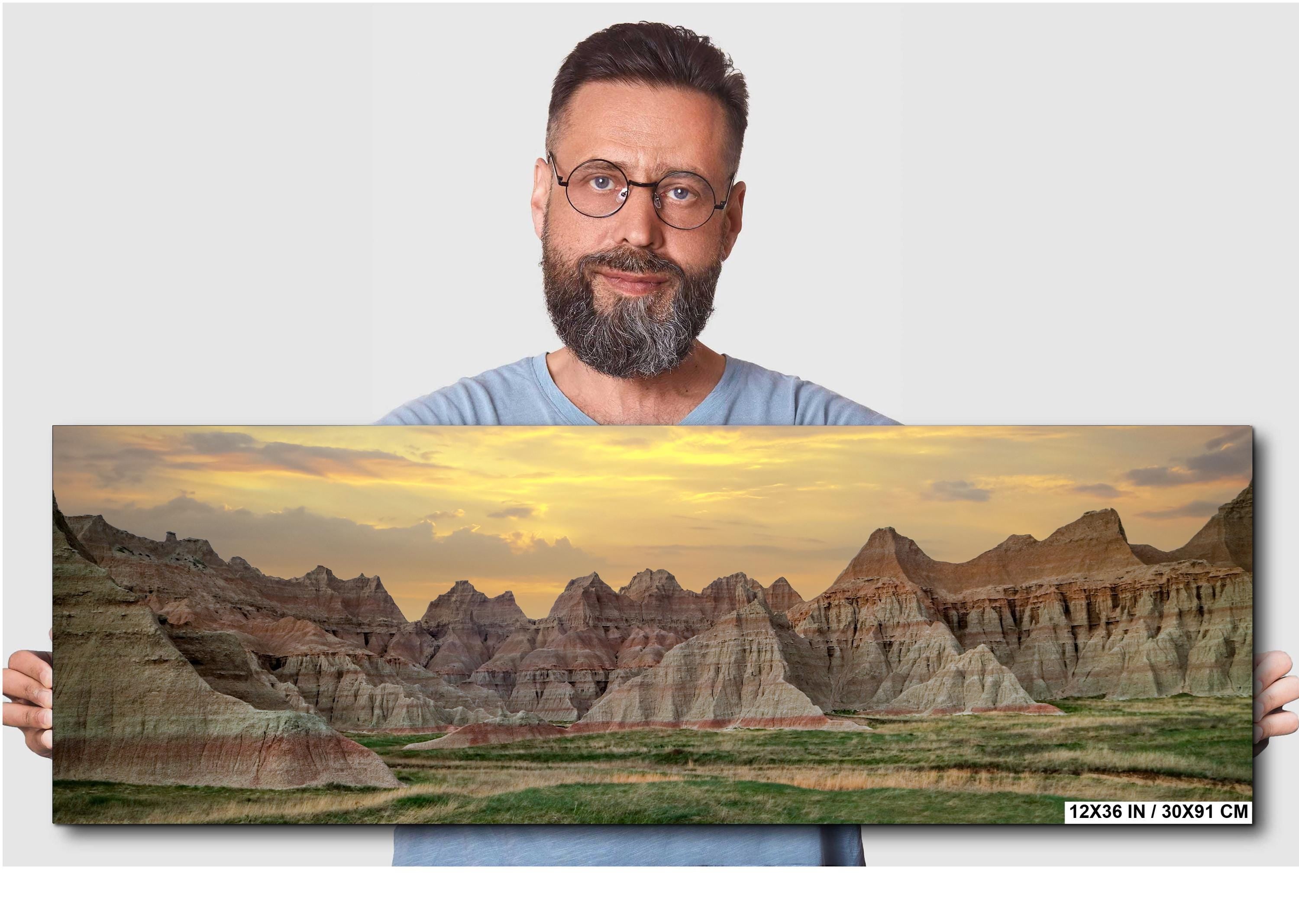 Man holding a panoramic landscape print of a desert scene with mountains.