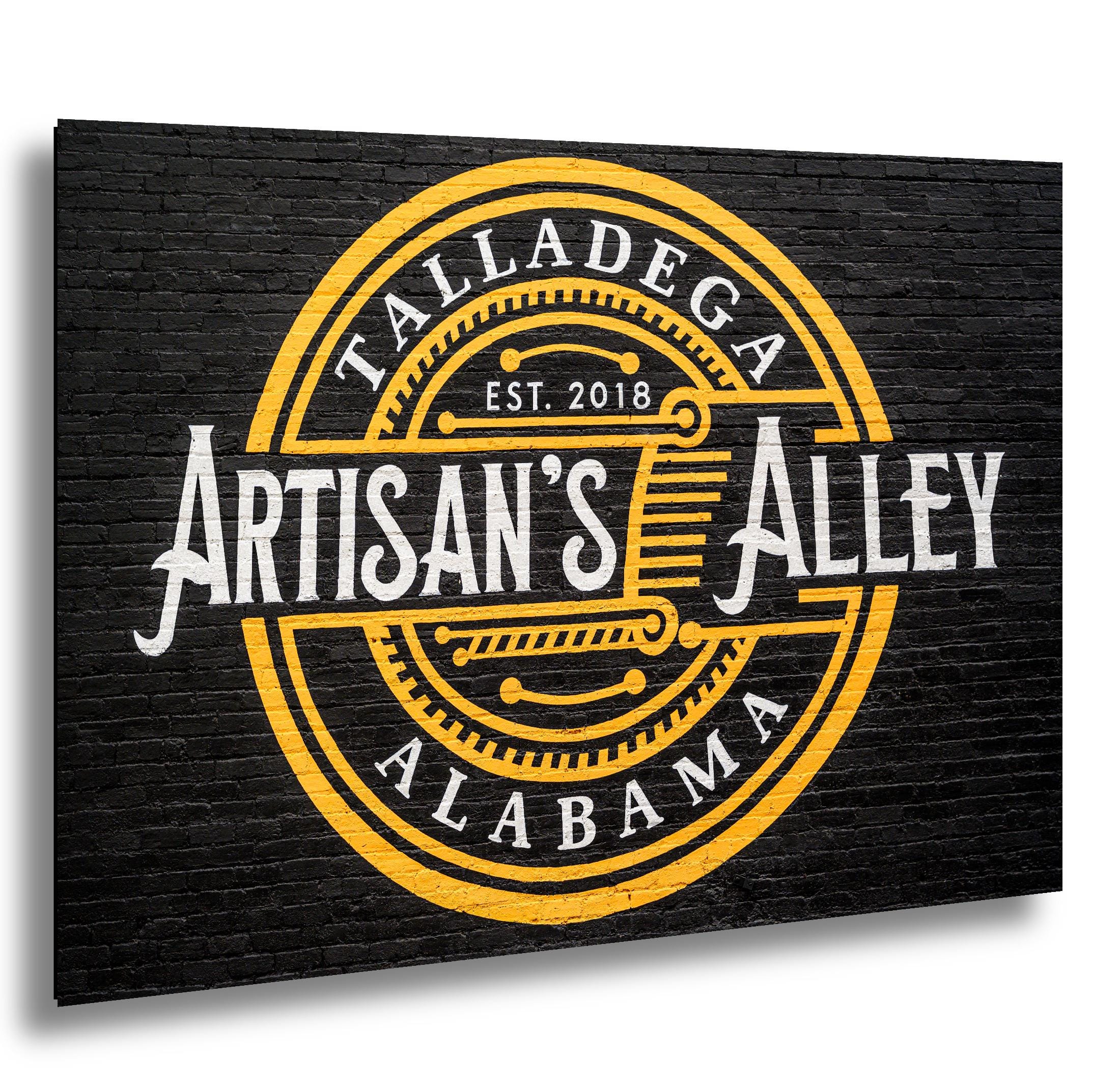 Artisan’s Alley mural in Talladega, Alabama, painted in gold and white on a black brick wall.