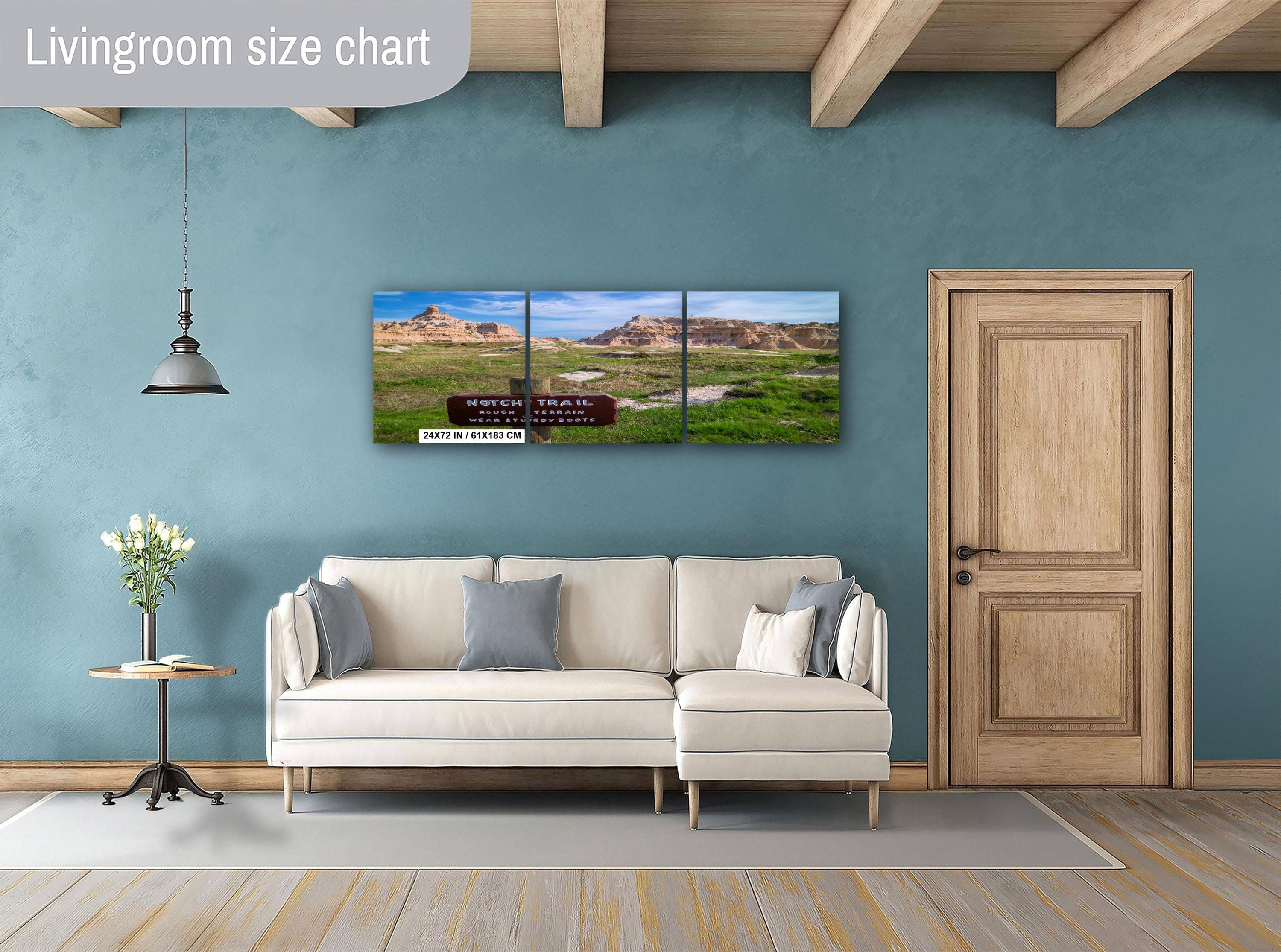 Living room with a beige sofa, decorative pillows, a side table with a plant, and a large wall-mounted triptych landscape painting.