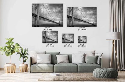 A black and white photograph of the Mackinac Bridge, capturing the engineering and grandeur of the structure with a backdrop of overcast sky and a body of water.