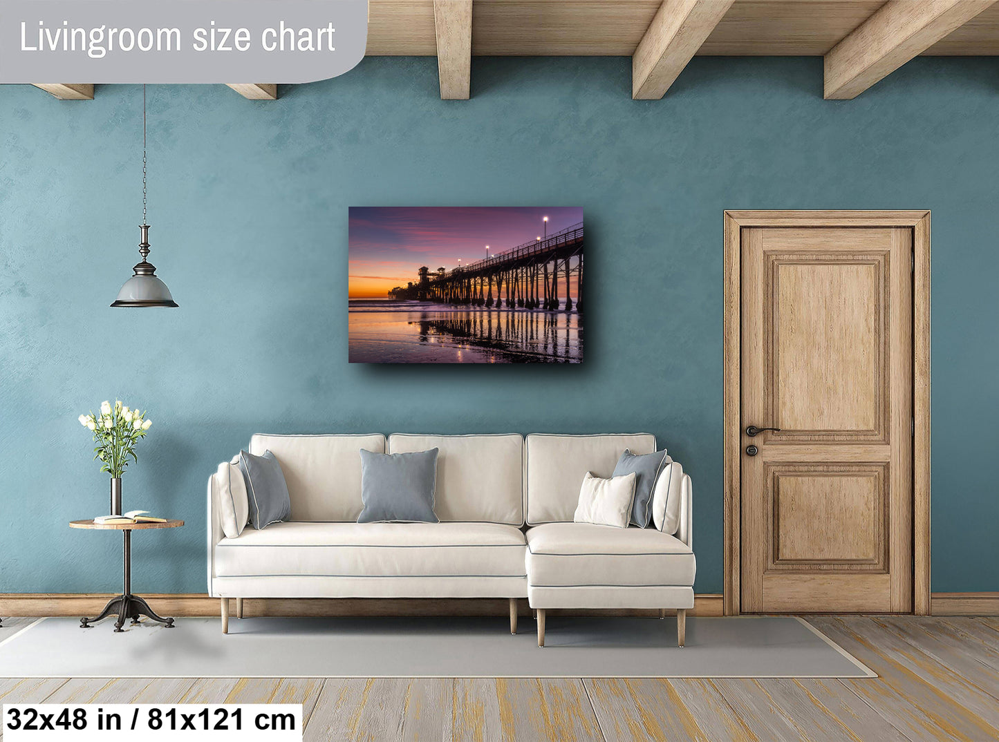 a living room with a large white sofa, a wooden door, and a painting of a bridge at sunset on the wall.