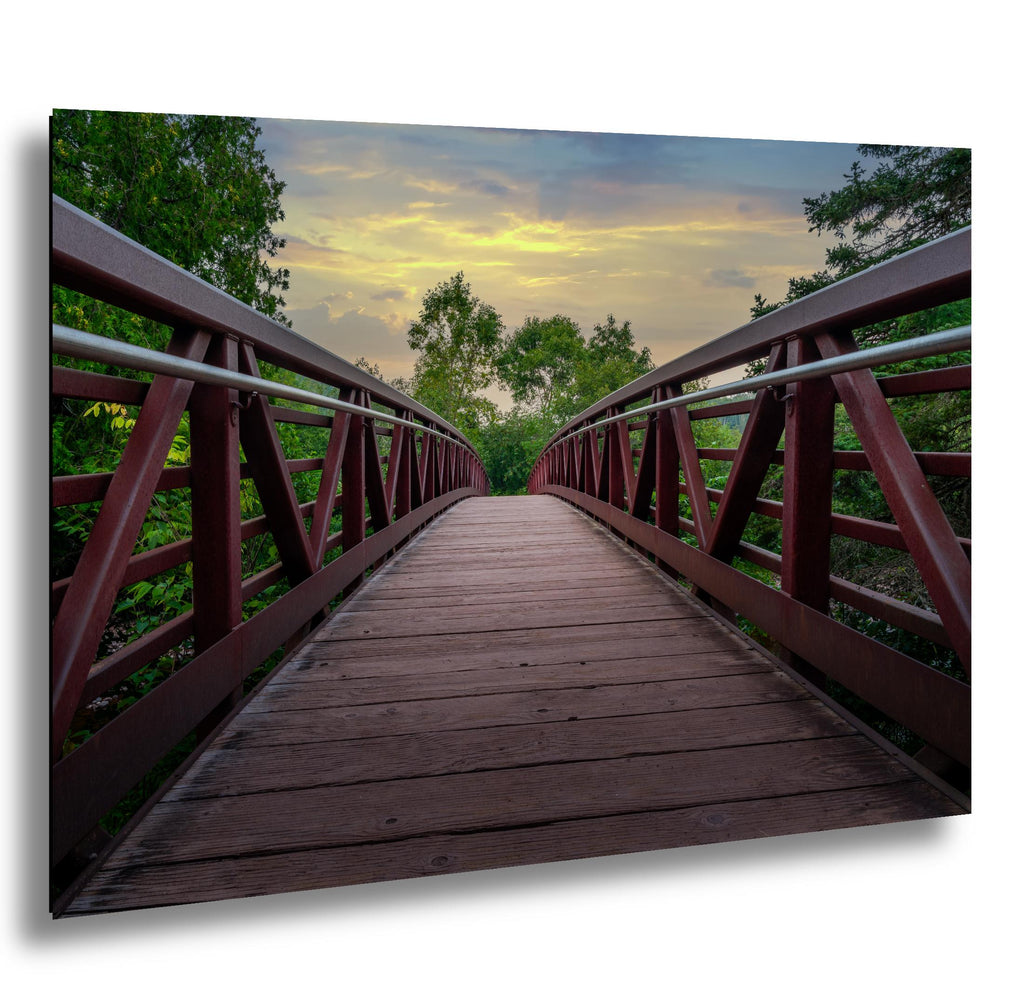 Rust-red footbridge at sunset leading through green trees in Gooseberry Falls State Park.