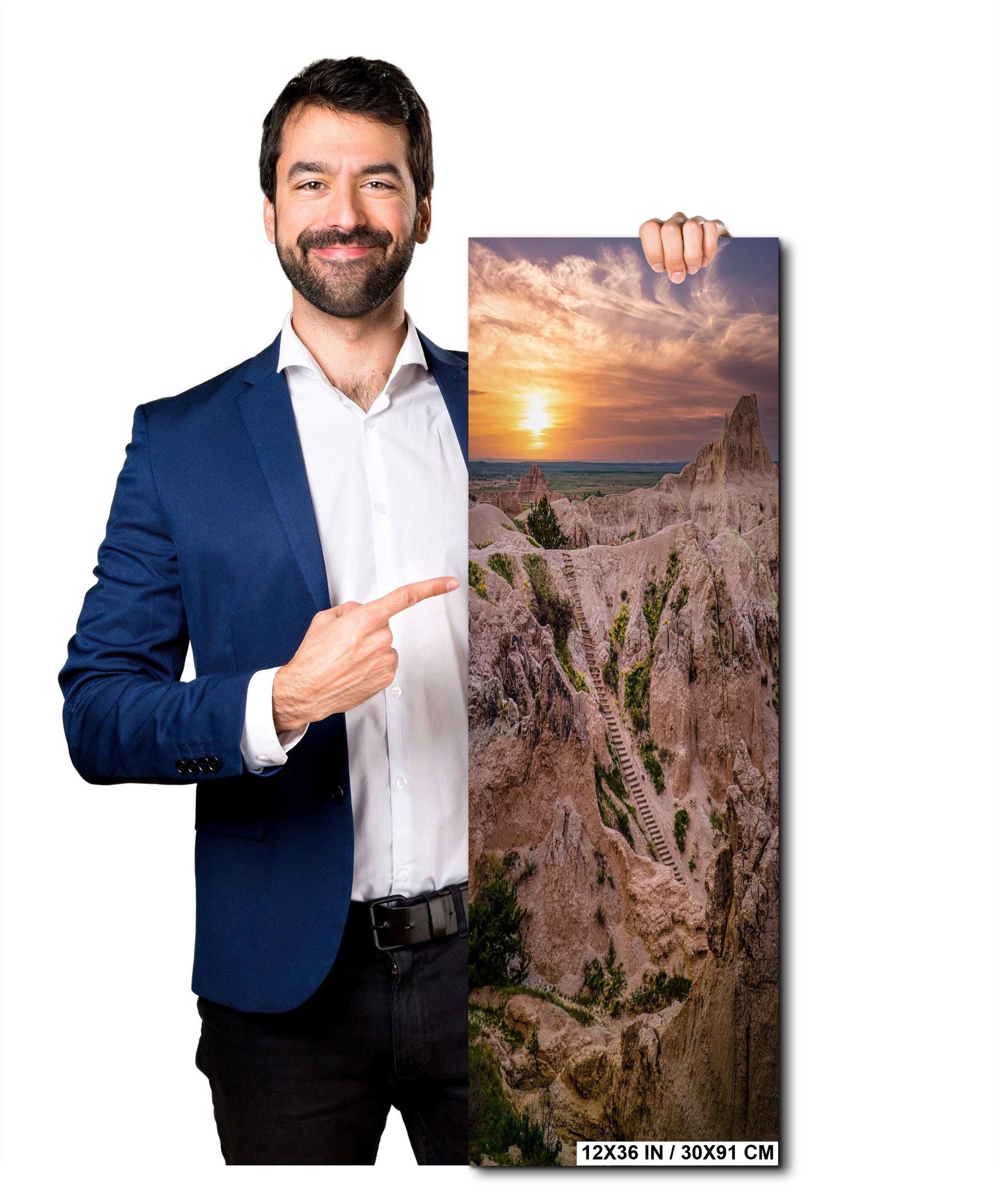 Man holding a canvas print of a scenic landscape with a sunset.